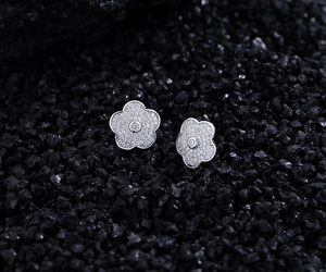 Gros plan sur des boucles d'oreilles camélia pavées de zircons sur pierre sombre