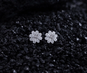 Macro shot of 925 silver daisy stud earrings with micro-pave crystals on black rock