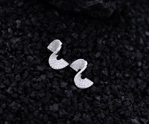 Macro detail of curved silver earrings with pavé set cubic zirconia on black stone texture