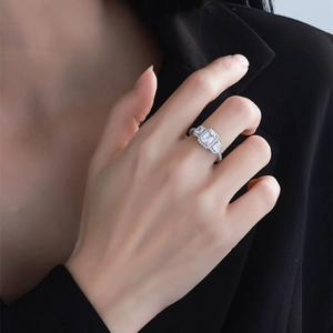Three-stone emerald-cut silver ring with halo setting on a model wearing black suit