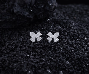 Macro shot of silver bow stud earrings with micro-pave zircons on black volcanic rock