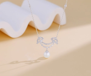 Macro detail of silver necklace with diamond-encrusted bow pendant and round white pearl