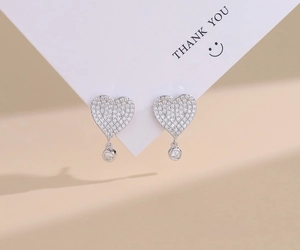 Detail of heart-shaped S925 silver stud earrings with pavé micro-set diamonds on a card