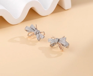 Macro detail of S925 silver bow stud earrings with cubic zirconia and rose gold rope accents