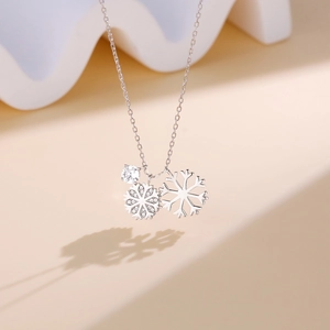 Silver double snowflake pendant necklace with sparkling cubic zirconia on a white wave stand