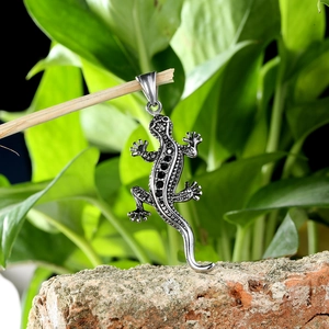 Pendentif gecko lézard en acier avec pierres noires sur un décor naturel de plein air