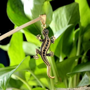 Pendentif gecko doré avec pierres noires suspendu sur une branche d'arbre naturelle