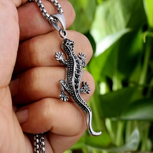 Gros plan du pendentif gecko argenté avec pierres noires et chaîne en perles carrées