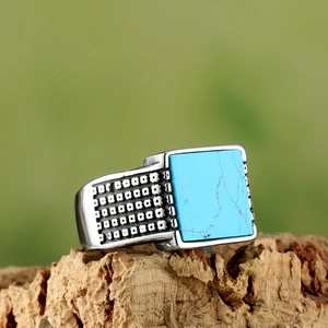 Detailed macro of vintage mens square turquoise ring on natural wood texture background