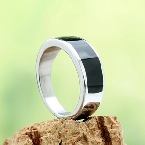Detailed close-up of a silver stainless steel ring with black epoxy inlay on tree bark