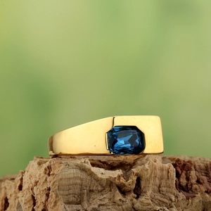 Close-up of a wide gold ring with a rectangular blue gemstone on a natural bark base
