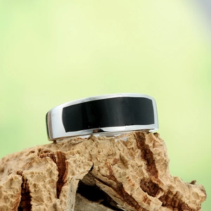 Close-up of a wide stainless steel band ring with a black enamel rectangle on a bark texture