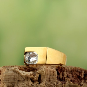 Detailed view of a gold wide band signet ring with a large rectangular zircon on wood