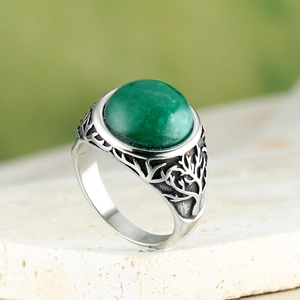Macro shot of silver ring featuring a green emerald-style gemstone and tree of life carving