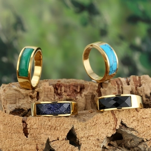 Stainless steel gold rings set with green, blue, and black gemstones on wood