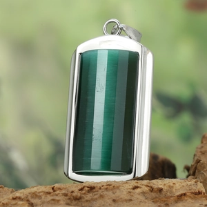 Detail shot of rectangular green cat eye pendant on wood with blurred nature background