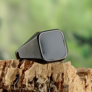Bague chevalière carrée en acier inoxydable noir poli sur un fond de bois naturel