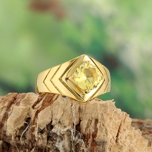 Detailed macro shot of a gold-finish ring with a yellow stone on natural bark