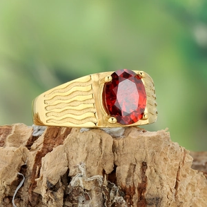 Macro shot of gold-plated wavy ring featuring an oval red gemstone on natural bark
