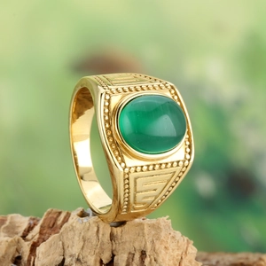 Macro shot of gold-plated signet ring with green oval gemstone and geometric patterns