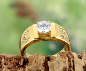 Gros plan sur une bague large dorée avec un grand zircon rond serti de quatre griffes