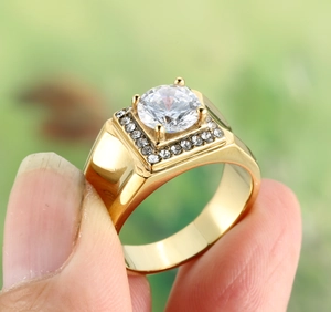 Détail d'une bague dorée avec pierre centrale ronde et halo carré de petits diamants