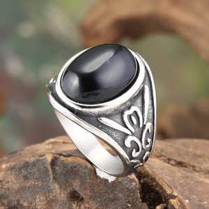Vintage stainless steel ring with black oval gemstone and floral relief on wood base