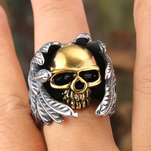 Punk style stainless steel ring with golden skull and silver wings shown on finger