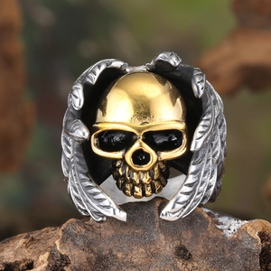 Detail of a punk skull ring with golden face and silver wing carvings on a wood base