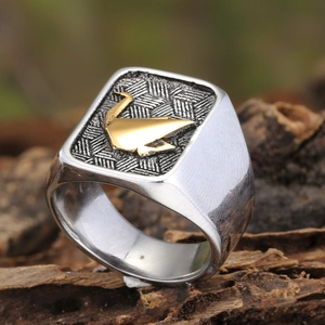 Détail macro d'une bague chevalière en acier avec grue dorée et motif tissé