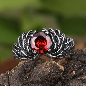 Macro shot of retro silver wing ring with deep red gemstone on natural bark background