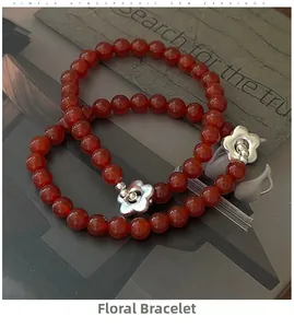 Detail of red agate bead bracelet set with silver flower charms on vintage paper