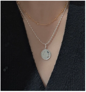 Close-up of a layered star necklace with an engraved coin pendant on a black garment