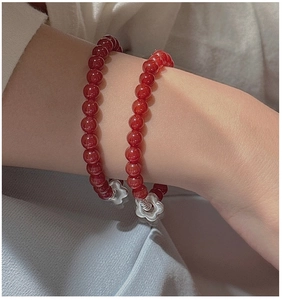 Close-up of red agate flower bracelet with silver charms in a layered jewelry look