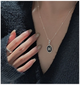 Dettaglio di un ciondolo H in argento sterling con smalto nero su una collana a sfere