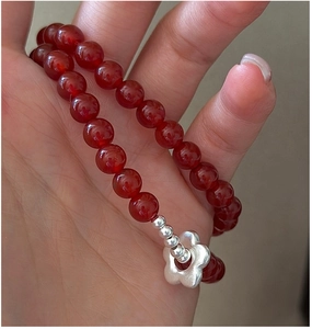 Detail of red agate beads and S925 sterling silver flower charm on a minimalist bracelet