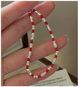 Close-up of hand-woven red rope bracelet with silver fish charms and adjustable clasp