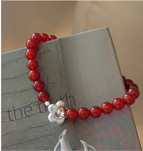Macro shot of red agate beads bracelet with silver flower charm on green box