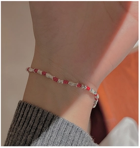 Close-up of hand-woven red string bracelet featuring silver fish charms and metal beads