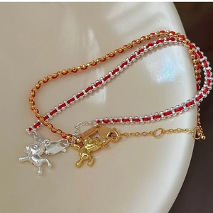 Dettaglio di bracciali intrecciati rossi con ciondoli di animali in argento e oro su ceramica
