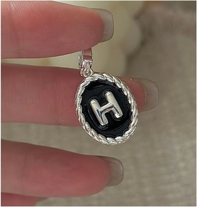 Dettaglio del ciondolo ovale in argento S925 con smalto nero e lettera H in rilievo