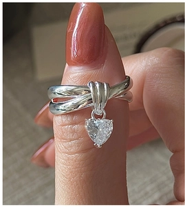 Detailed close-up of a silver intertwined ring featuring a dangling heart-shaped zircon