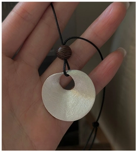 Macro detail of S925 sterling silver brushed metal disc pendant with wood bead on black cord