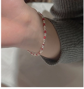Macro detail of a red woven rope bracelet with S925 silver fish charm on model wrist