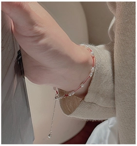 Gros plan d'un bracelet en fil rouge et perles porté sur un pull en maille beige