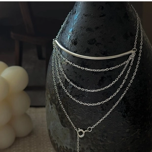 Macro detail of silver S925 tiered tassel necklace with multiple layered chains on a vase