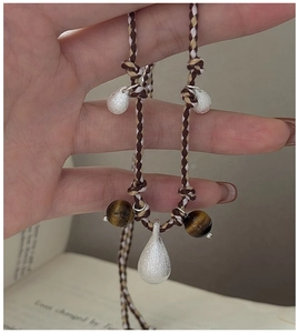 Detailed shot of silver water-drop pendant with tiger eye beads on woven cord