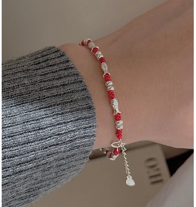 Detail of red braided silver bracelet with fish charms worn on a woman's wrist