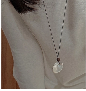 Close-up of shell pendant necklace with wood bead on white sweater for casual style