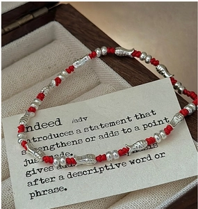 Detail of S925 sterling silver fish charms on a hand-woven red cord bracelet